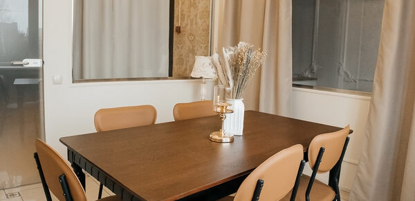 Open Space (Открытое пространство) для мероприятий. Столовая зона с большим деревянным прямоугольным столом и шестью бежевыми стульями на металлических ножках. На столе белая ваза с сухоцветами и подставка с лампой. Светлые стены с панелями, бежевые шторы, застекленная дверь. Пол плиточный белый с узором.