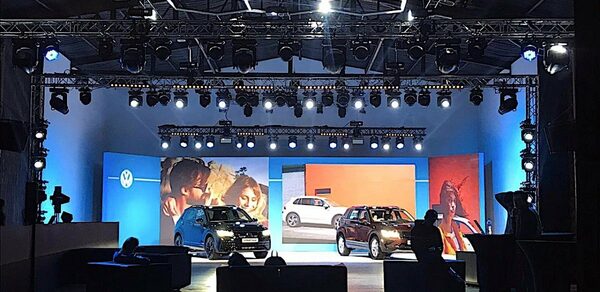 Studio Hall(Студио Холл). Пространство для мероприятий с автомобильной экспозицией, сцена окружена светодиодными экранами, мягкая мебель и барные столы, подвесные конструкции освещения, синий и оранжевый цвета, черный и белый автомобили, несколько проекционных световых приборов.