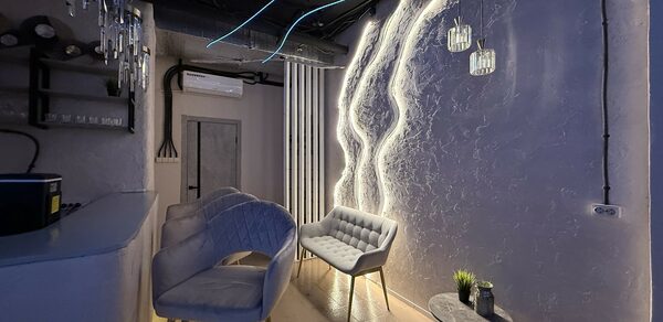 Лофт SUNRISE(Восход Солнца). Просторное помещение на 15 гостей. Небольшое помещение с декоративной стеной и неоновым освещением. Барная стойка с барными стульями. Мягкие кресла и круглый столик с растением. Подвесные светильники. Потолок с декоративной проводкой и вентиляцией. Стены текстурированные.