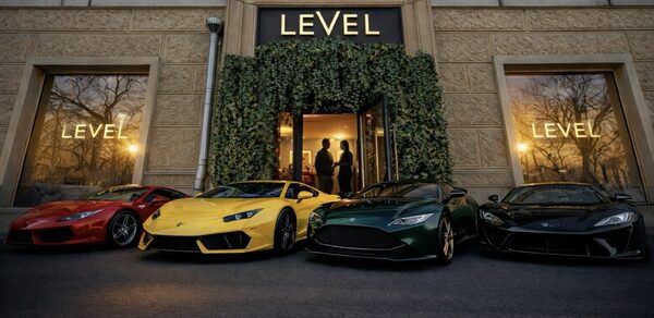 Level 5(Лэвел 5). Фасад здания с большими окнами, текст "LEVEL" над входом и на оконных витринах, стены из текстурного камня, зелёные растения обрамляют вход. Перед входом припаркованы спортивные автомобили красного, жёлтого, зелёного и чёрного цветов.