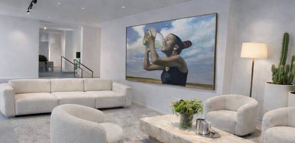 Level 5(Лэвел 5). Современное помещение с белыми стенами и ковролином. Мебель: угловой диван и три круглых кресла светлого цвета, прямоугольный журнальный столик. На стене большая картина, рядом напольный светильник и зелёные растения. Потолочные точечные светильники.