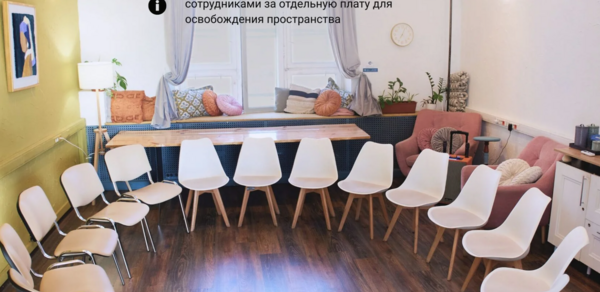 H4U. Светлый зал П-602. Круговая расстановка из пятнадцати белых стульев с деревянными ножками в светлом помещении с деревянным полом. На окне серые занавески, на стенах картины и часы. Справа розовый диван и стол с элементами декора. Текстура белых и зеленых стен.