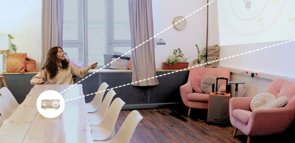 H4U. Светлый зал П-602. Просторная комната с большим деревянным столом и белыми стульями. По бокам розовые кресла с подушками. На стене проекция, окна закрыты шторами. На подоконнике растения. Деревянный пол, стены светлые. Настенные часы.