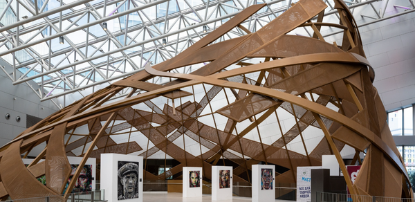Кунцево Плаза. Просторное помещение с причудливой деревянной конструкцией под стеклянной крышей. Белые стенды с портретами расположены по кругу. Пол светлый, стены белые. Видна надпись "Maгия".