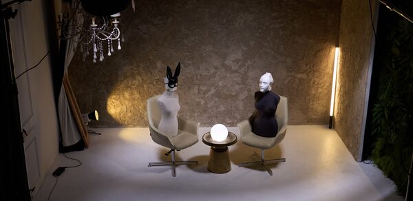 WhiteFox Studio(Студия Белая Лиса). Помещение с двумя креслами и круглым столиком между ними, на котором светится шар. На креслах находятся манекены. На стене серая текстурная поверхность, светодиодная лампа стоит вертикально справа. Светлый пол и подвесная люстра.