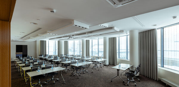 Конференц-зал Экспресс Махараджей. Просторное конференц-помещение с отдельными столами и черными стульями. Белые стены и потолок с встроенным освещением. Большие окна с жалюзи, панорамный вид. Ковровое покрытие коричневого цвета. Установлен кондиционер.