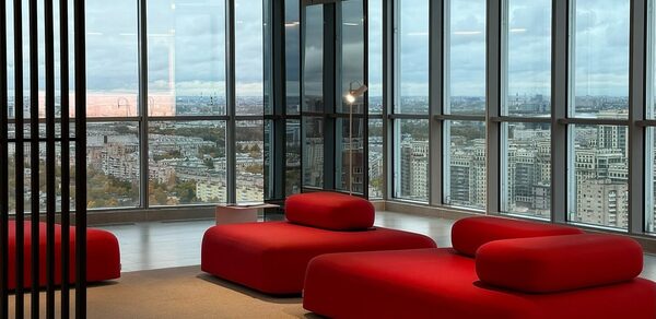 Арт-Плейс Фактура. Современный лофт с видом на весь город. Современное помещение с окнами от пола до потолка, открывающими вид на город. В интерьере красные мягкие диваны и бежевый пол. Потолочные светильники обеспечивают искусственное освещение. Декор из стекла и металла.