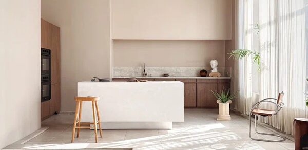 Киото. Светлый зал с кухней. Кухонное пространство с островом и барным стулом, деревянные шкафы, встроенная техника, мраморная столешница, светло-бежевые стены, большое окно с легкими шторами, стеклянный стул, растения в горшках, светлое плиточное покрытие.