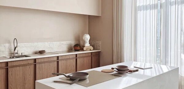 Киото. Светлый зал с кухней. Кухонное пространство с белым островом в центре, деревянными шкафами, мраморной столешницей и раковиной. Светлые шторы от пола до потолка. На столе посуда и кухонные принадлежности. Светлые нейтральные стены.