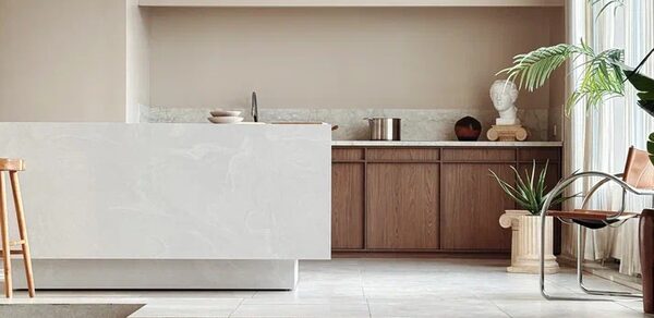 Киото. Светлый зал с кухней. Современное пространство с кухонной зоной. Белая мраморная барная стойка, светло-коричневые деревянные шкафы, металлический стул с кожаным сиденьем. Горшечные растения и бюст на колонне. Светлые тона, обилие естественного света.