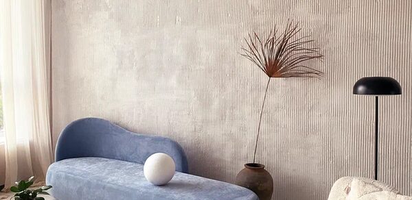 Киото. Светлый зал с кухней. Просторная комната с высокими потолками и светлыми стенами. Голубой диван округлой формы, рядом керамическая ваза с растением и лампа с черным абажуром. Светлые занавески пропускают естественный свет. Пол светлый, на нем стоит стол и растение.