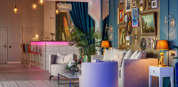 Лофт Май. Стильное пространство с верандой. Гостиная с баром в современном стиле. Белые диваны и кресла, стол с цветами. На стене множество картин и зеркал в рамах. Бар с высокими стульями и розовой подсветкой. Потолочные лампы, декоративные растения, синие шторы. Стены бирюзовые, полы плиточные.