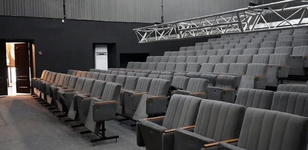 Театр в Хамовниках. Аудитория с рядовой расстановкой серых кресел. Настенное покрытие и пол темные. Освещение отсутствует, видны металлические конструкции для светового оборудования. Открытая дверь на заднем плане.