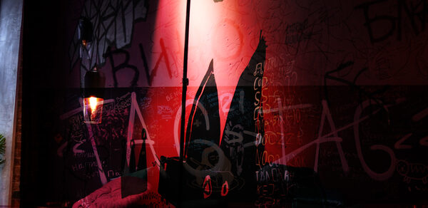 Винный бар “Дело не в вине”. Темное помещение с граффити на стенах, розово-красное освещение. Видны подвесные светильники с лампочками Эдисона. На переднем плане подушка и декоративный элемент в виде черного кролика с большими ушами.