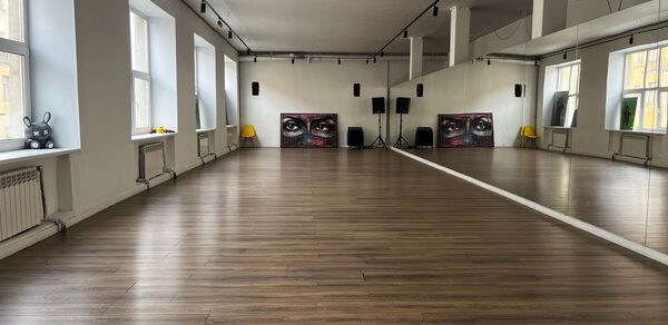 The Flow Space(Пространство Поток). Просторное помещение с деревянным полом, зеркалами вдоль одной стены. Белые стены, большие окна, обеспечивающие естественное освещение. Акустическая система и картины на задней стене. Потолочные светильники и несколько жёлтых стульев.