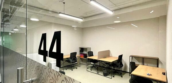 Smart Coworking(Умный Коворкинг). Офисное помещение с четырьмя рабочими местами, разделёнными столами и стульями на колёсиках. Стеклянная дверь с надписью «44». Освещение из подвесных светильников. Светлые стены и пол. Открытые потолочные коммуникации.