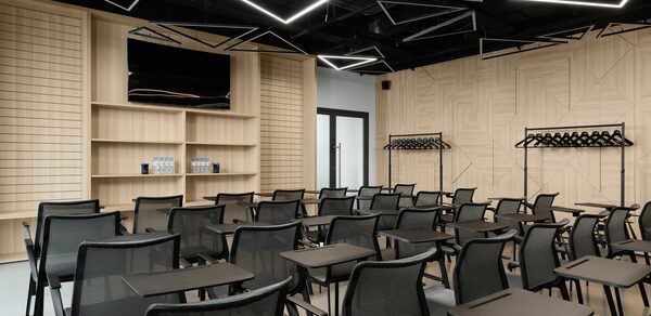 YES Technopark(ДА Технопарк). Конференц-зал. Конференц-зал с рядами черных стульев и откидными столиками, деревянные стены с геометрическим узором, открытые гардеробные стойки, потолочные светильники геометрической формы, телевизор на полке, бутылки с водой рядом.