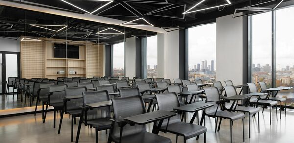 YES Technopark(ДА Технопарк). Конференц-зал. Конференц-зал с рядами серых стульев с пюпитрами, большие окна с видом на город, черный потолок с геометрическими светильниками, пол из светлого дерева, на стене зеркало и экран.