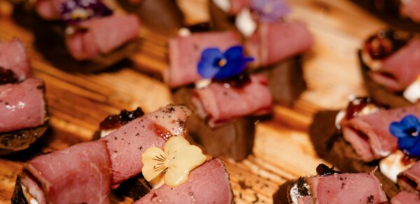 Атлас. Мультиформатная площадка. Маленькие закуски из рулетов мяса на деревянной поверхности, украшенные съедобными цветами.