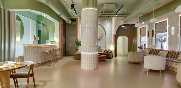 SOK SPACE (Сок Пространство). Лофт Октябрь. Современное просторное помещение с барной стойкой, высокими стульями, круглыми столами и мягкими креслами. Центральная колонна облицована плиткой. Светлые пастельные тона, декоративные панели на стенах, подвесные светильники и встроенное потолочное освещение.