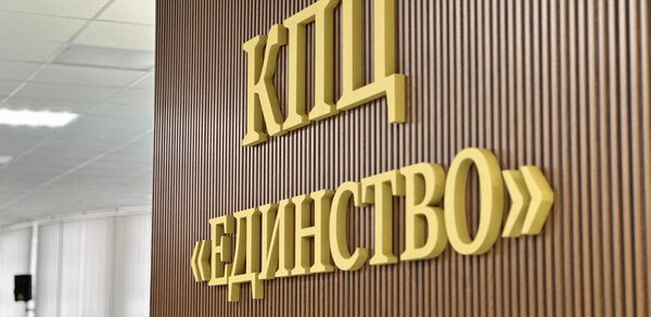 КПЦ Единство. Текст на стене: "КПЦ ЕДИНСТВО". Стена из вертикальных деревянных панелей коричневого цвета. Потолочные светильники с ровным мягким освещением. Белые потолочные панели.
