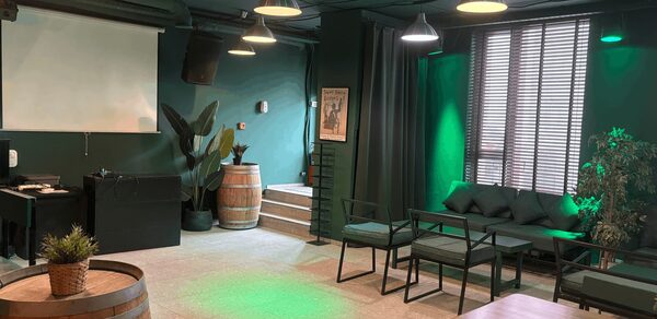 Work Shop Loft(Воркшоп Лофт). Зал 11 . Просторная комната с темно-зелеными стенами, большими окнами и жалюзи. Мебель: диваны, стулья, деревянные бочки, столы. Освещение представлено подвесными светильниками. На стене проекторный экран. В углу растения, постер на стене.