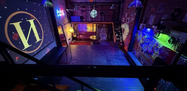 Лофт ИЗНАНКА. Зал ЛИХИЕ 90-е. Затемнённая комната лофта, много людей в кадре проводят фуршетное мероприятие, беря еду с объединённых столов. Несколько людей на кадре танцуют