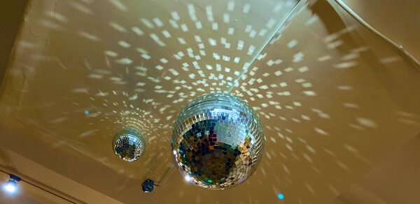 Лофт для вечеринок с коктейльным баром . Потолок с зеркальными диско-шарами, создающими световые узоры. Светло-бежевые поверхности. Видна электропроводка. Есть встроенные светильники.