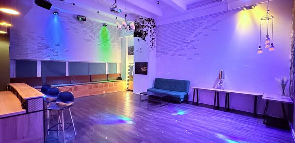 Barshowplace (БарШоуПлейс). Лофт для вечеринок с коктейльным баром . Пространство для мероприятий с деревянным полом, барной стойкой и высокими стульями. Стены декорированы цветным подсветкой, на потолке подвесные лампы. Имеются диваны, столики, велюровая обивка мебели. Настенные элементы из белого кирпича и древесины.