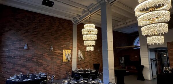 Geo loft (Гео Лофт). Кирпичный лофт с большими окнами. Праздничное пространство с кирпичными стенами, круглые столы с черными скатертями и сервировкой, металлические стулья, две большие хрустальные люстры, декоративные картины, высокие потолки, колонны, затемненное освещение, фуршетные столы.