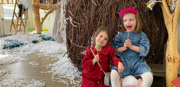 Children's eco-loft. Деревянное праздничное пространство с парой детей. Комната украшена ветками и бумажными лентами. На фоне деревянные конструкции и лестница. Яркие воздушные шары. Пол светло-коричневого цвета.