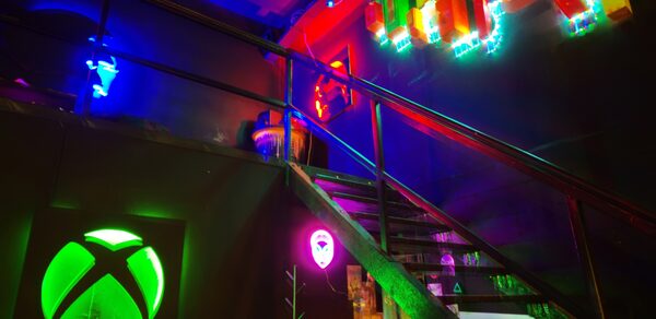 Лофт Геймеры. Лестница на второй этаж, под ней неоновая подвеска с игровым логотипом и неоновая лампа. 