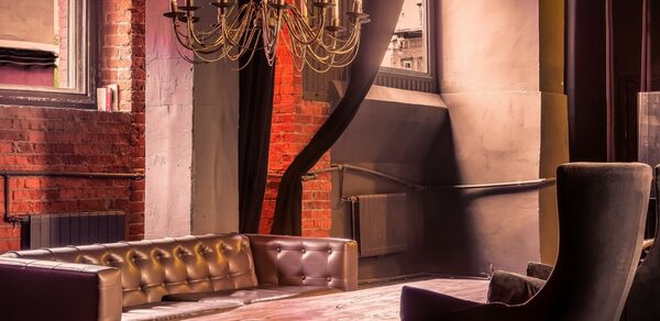 Music loft (Мьюзик лофт). Лофт-пространство с кирпичными стенами, деревянным столом и кожаными диванами. Над столом висит металлическая люстра с имитацией свечей. Кресло с высокой спинкой стоит рядом. Окно со шторами пропускает мягкий свет.