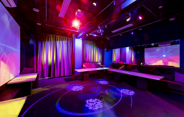 Зеркальный Лофт с Караоке и светомузыкой. Караоке-зал с приглушенным освещением. Зал меблирован диванами и столами, большие зеркала на стенах. На полу световые эффекты в виде узоров. Занавески в ярких цветах, разноцветные прожекторы, темно-синий интерьер.