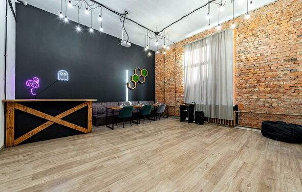 Rubin Loft (Рубин Лофт). Лофт средний. Лофт с деревянным полом, кирпичными стенами и черным потолком. Барная стойка, диван и стулья. Неоновая вывеска на стене. Подвесные светильники и светодиоды. Легкие шторы на окне. Декор в виде сот. Черные мешки для сидения.