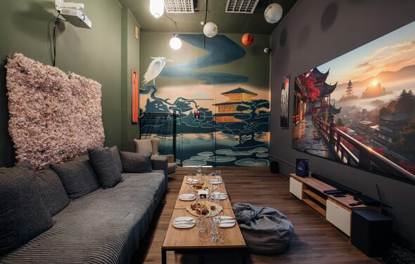 Зал Китай. Лофт-зал в китайском стиле . Караоке-зал с диваном и креслом у стены в зелёных тонах, настенной росписью с азиатскими мотивами, столом с закусками и напитками, пуфом. Большой экран с изображением природы, мягкое освещение потолочными светильниками, деревянный пол.