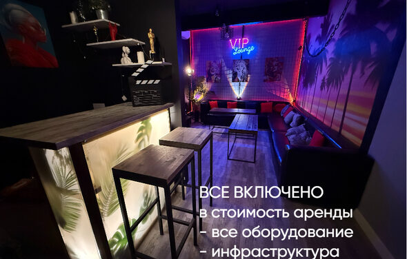 Лофт ИЗНАНКА. Зал ГОЛЛИВУД. Лаунж-зона с барной стойкой и высокими стульями, мягкими диванами вдоль стены, неоновая надпись "VIP Lounge", декоративная подсветка, изображения на стене, пол темный и деревянный, надпись "ВСЕ ВКЛЮЧЕНО".