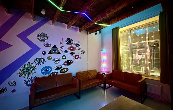 Яркий двухуровневый лофт. Приглушённый свет. Диваны. Стена с рисунками. Окно со светящейся гирляндой