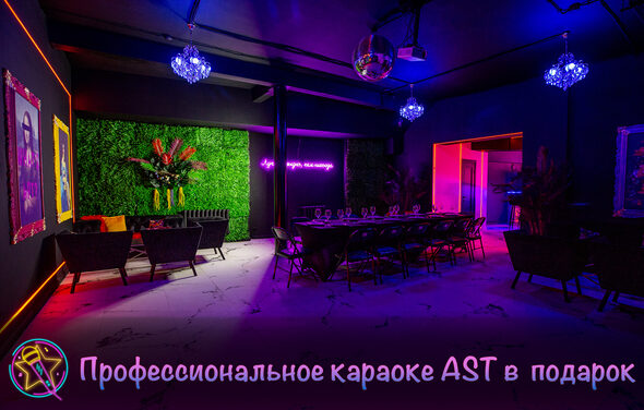 Белый неоновый лофт-зал. Зал для мероприятий с мебелью из плетёных кресел и длинного стола, окружённого стульями. На стене неоновая надпись, рядом зелёная живая стена с цветами. Потолок украшен диско-шаром и люстрами. Освещение цветное, приглушённое. На стенах картины.