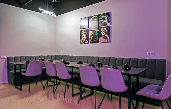 Лофт-зал с караоке и диско-шаром. Большая комната с Г-образным серым диваном вдоль стены, черный стол и несколько розовых кресел. Стена украшена картинами с изображением статуй. Потолок черный, освещение в виде современных ламп. Пол бежевый с глянцевой поверхностью.