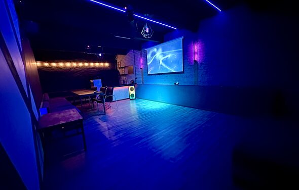 Kahovka loft (Каховка Лофт). Неоновый лофт-зал. Тёмное закрытое помещение с деревянным полом, напоминающее клуб или бар. На стене большой экран с проекцией, в комнате неоновая подсветка и диско-шар. Несколько столов и стульев у стены, светящаяся колонка.