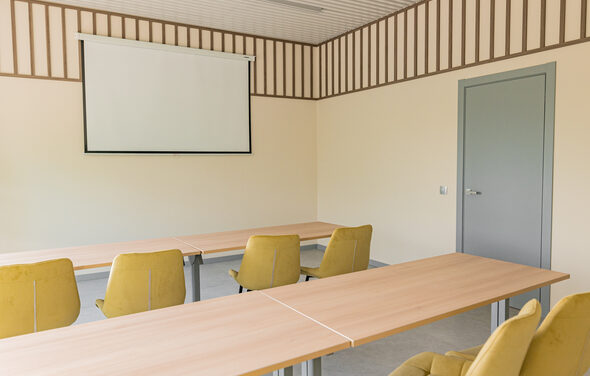 Зал 5. Светлый малый конференц-зал до 20 человек в Академии Кантаты. Просторная комната с бежевыми стенами и потолком с деревянными панелями. В центре расположены столы из светлого дерева и желтые стулья. На стене висит проекционный экран. Справа серая дверь. Естественное освещение.