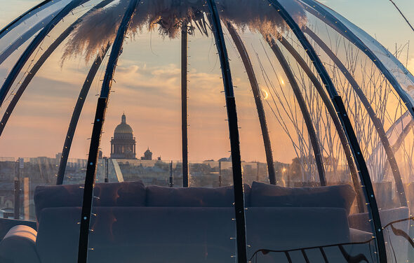 Sky Terrasse(Небо Терраса). Прозрачный купол с металлическим каркасом, внутри которого находится мягкий диван тёмного цвета. Купол украшен подсветкой и декоративными растениями сверху. За куполом виден городской пейзаж на фоне заката.