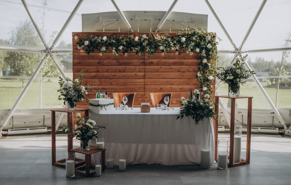 Эко-отель "Джао Да!Ча". Шатер-Сфера. Купольное пространство с панорамными окнами. Деревянная панель с зеленью. Стол с белой скатертью, украшенный цветами и свечами. Два стула. Деревянные стоянья с цветами. Пол серый. Натуральные материалы, нежные цвета.