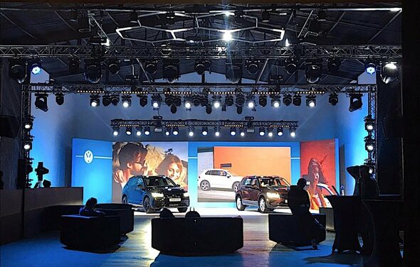 Studio Hall(Студио Холл). Пространство для мероприятий с автомобильной экспозицией, сцена окружена светодиодными экранами, мягкая мебель и барные столы, подвесные конструкции освещения, синий и оранжевый цвета, черный и белый автомобили, несколько проекционных световых приборов.