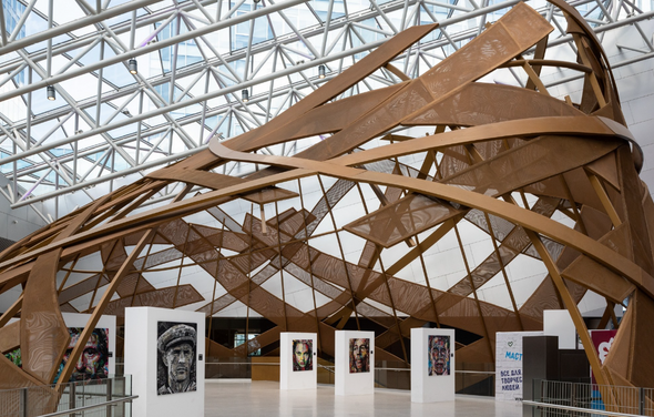 Кунцево Плаза. Просторное помещение с причудливой деревянной конструкцией под стеклянной крышей. Белые стенды с портретами расположены по кругу. Пол светлый, стены белые. Видна надпись "Maгия".