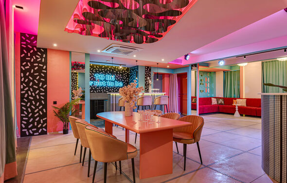 Лофт Шекспир. Стильный дизайнерский зал. Зал для мероприятий с ярким освещением, розовыми и бирюзовыми акцентами. Столы и стулья современных форм, барная стойка с высокими стульями. На стенах неоновая надпись. Декоративные панели с узорами, диваны с подушками. Потолок с декоративными элементами.