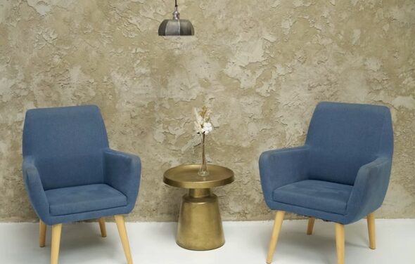 WhiteFox Studio(Студия Белая Лиса). Два синих кресла с деревянными ножками, маленький золотистый стол с вазой и сухими цветами между ними. Потолочный светильник над зоной, текстурная бежевая стена, белый пол.