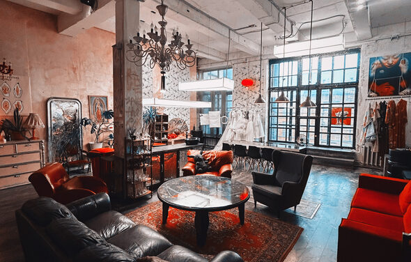 Лофт Делюкс. Лофт-пространство с высокой потолочной конструкцией и индустриальными окнами. Мебель: кожаные и мягкие кресла, круглые столы, комоды. Освещение: современные люстры и лампы. Декор на стенах, ковры на деревянном полу. Цвета: темный, красный, бежевый.