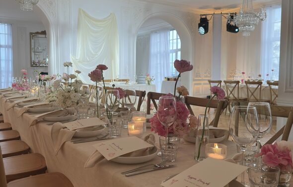 Арт-Плейс Фактура. Просторный лофт в классическом стиле. Белый банкетный зал с длинным деревянным столом, накрытым светлой скатертью. Установлены деревянные стулья. На столе стеклянная посуда, цветочные композиции, свечи. Белые стены, арочные окна, хрустальные люстры, текстильные драпировки.